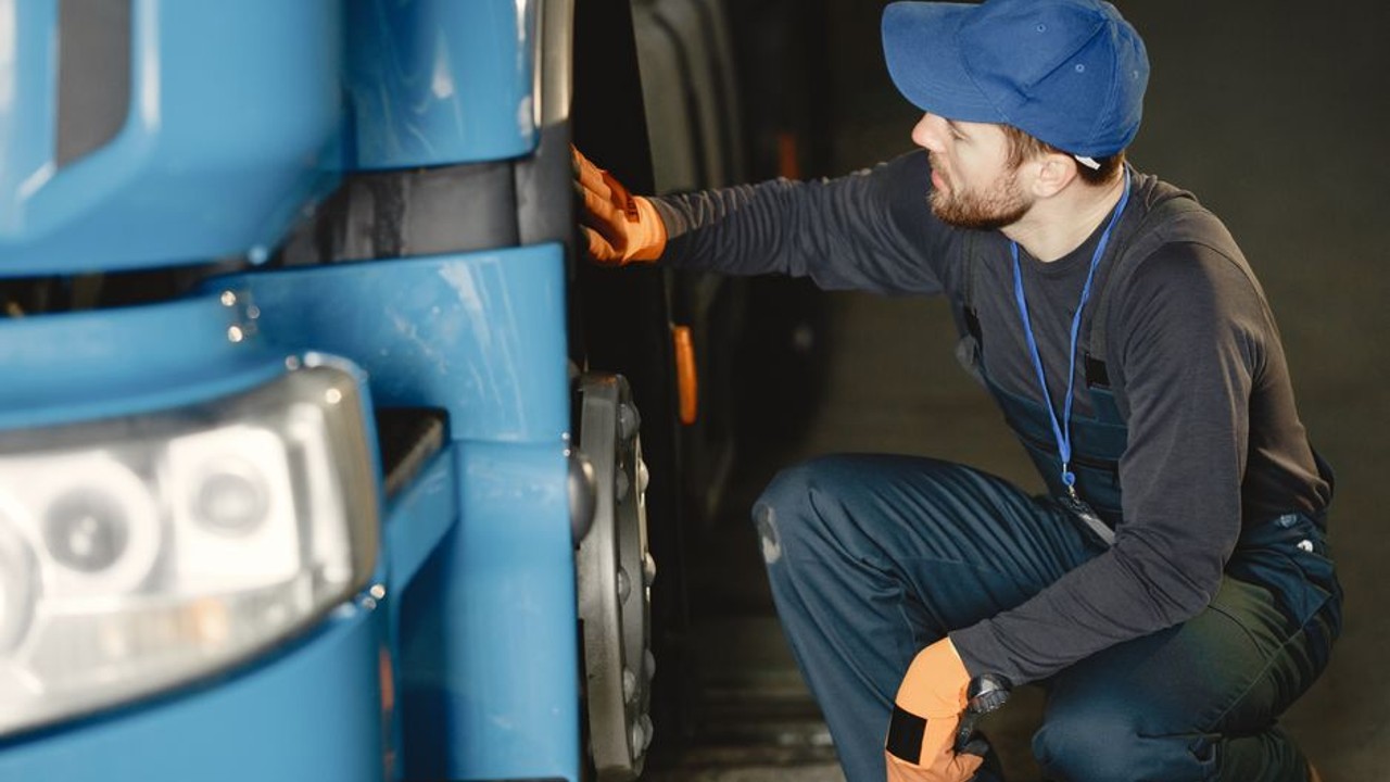 Professional truck driver checking tires during a stop, with a car carrier truck in the background, emphasizing safety and maintenance