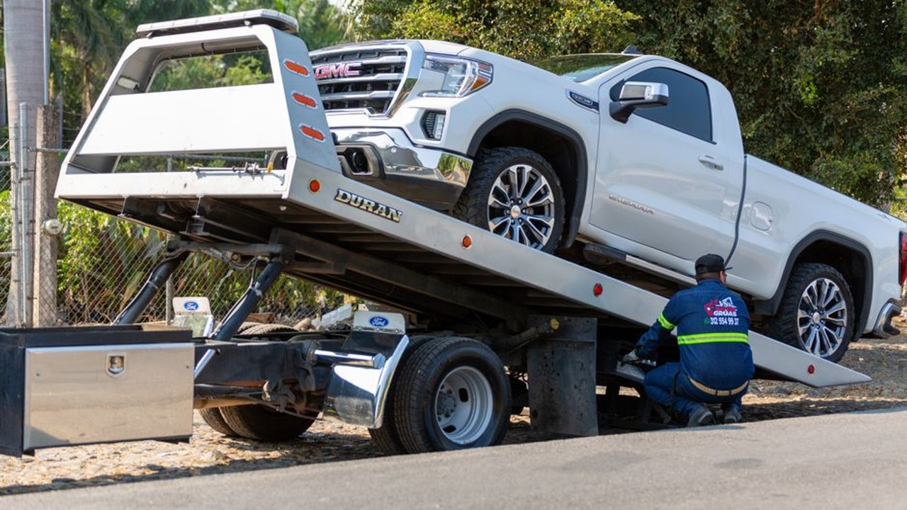 Car carrier truck with a flat tire pulled over safely on the shoulder of a highway, showing a roadside mechanical issue