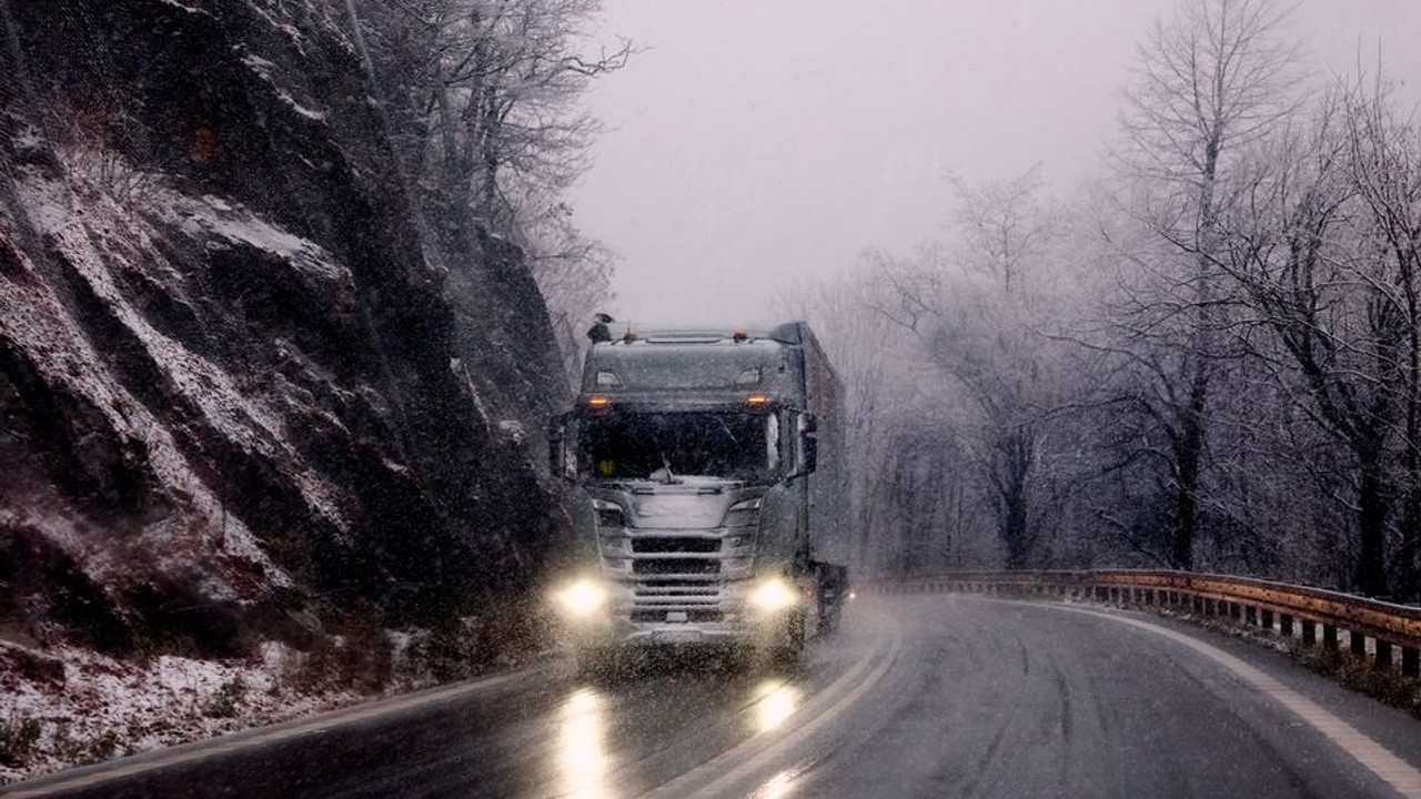 Large car carrier truck driving on a snow-covered highway during a winter storm, headlights cutting through falling snow.