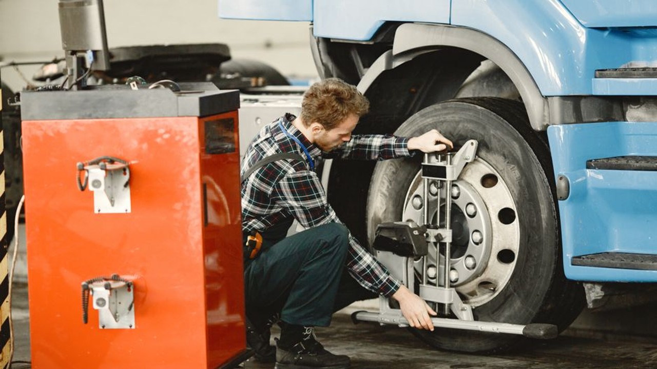 Professional truck driver checking the tires and undercarriage of an auto transport carrier during a roadside stop, ensuring safety.