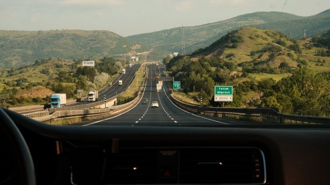 Person driving a car on a long, open highway with mountains in the background, showing the journey of a cross country drive.