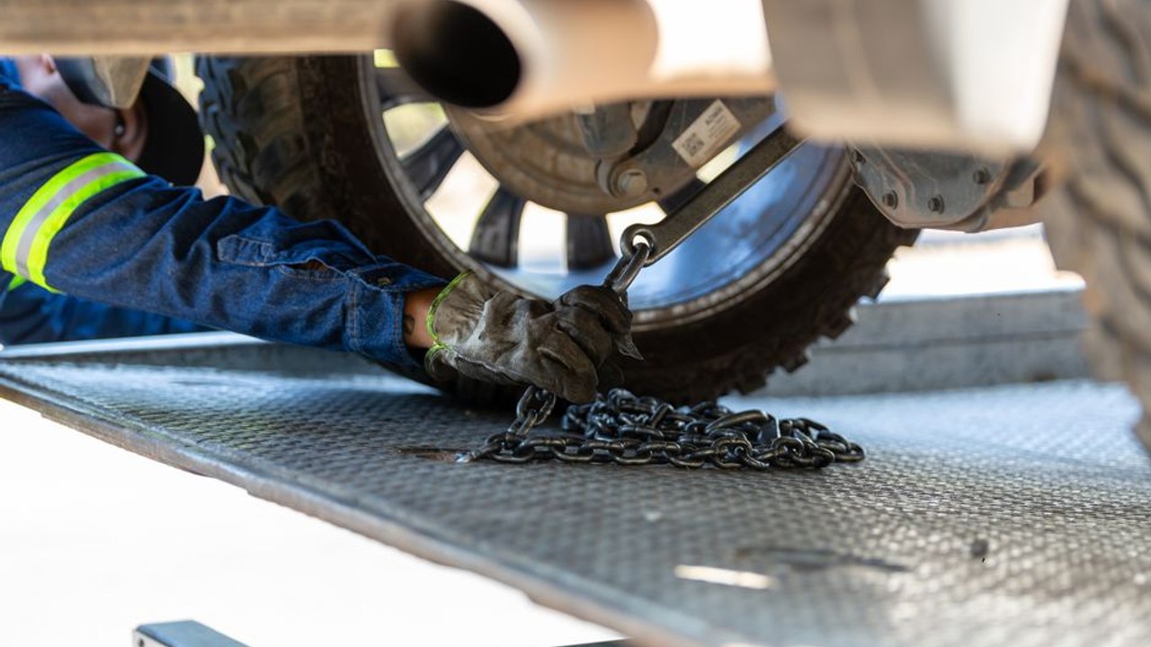 Professional car hauler securing a car onto an open auto transport trailer, ensuring safe and reliable vehicle transport.