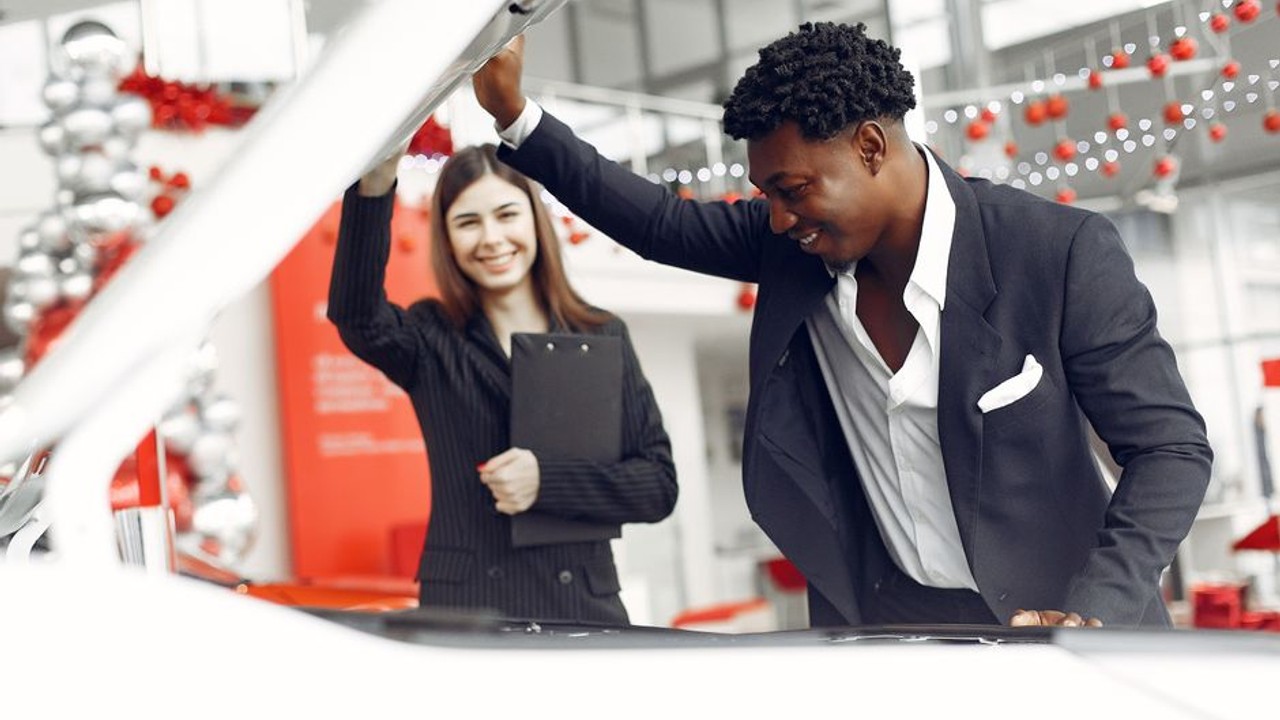 A family excitedly looking at a new car in a dealership showroom, considering a new purchase after a move.