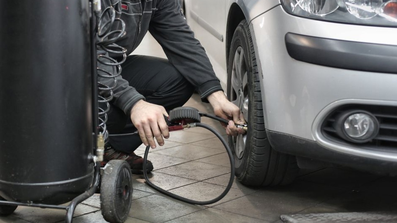 Professional mechanic checking tire pressure and battery terminals on a car being prepared for auto shipping.