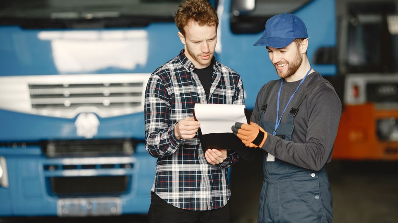 Car owner and truck driver performing a detailed pre-shipment inspection, documenting existing scratches and dents on the vehicle with a Bill of Lading.