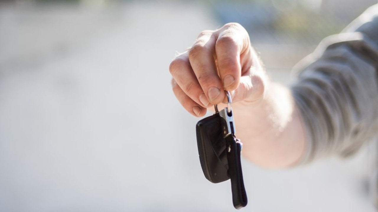 Car owner handing keys to a friendly car carrier driver during the pickup process for cross-country vehicle transport, with an empty car trailer in the background.