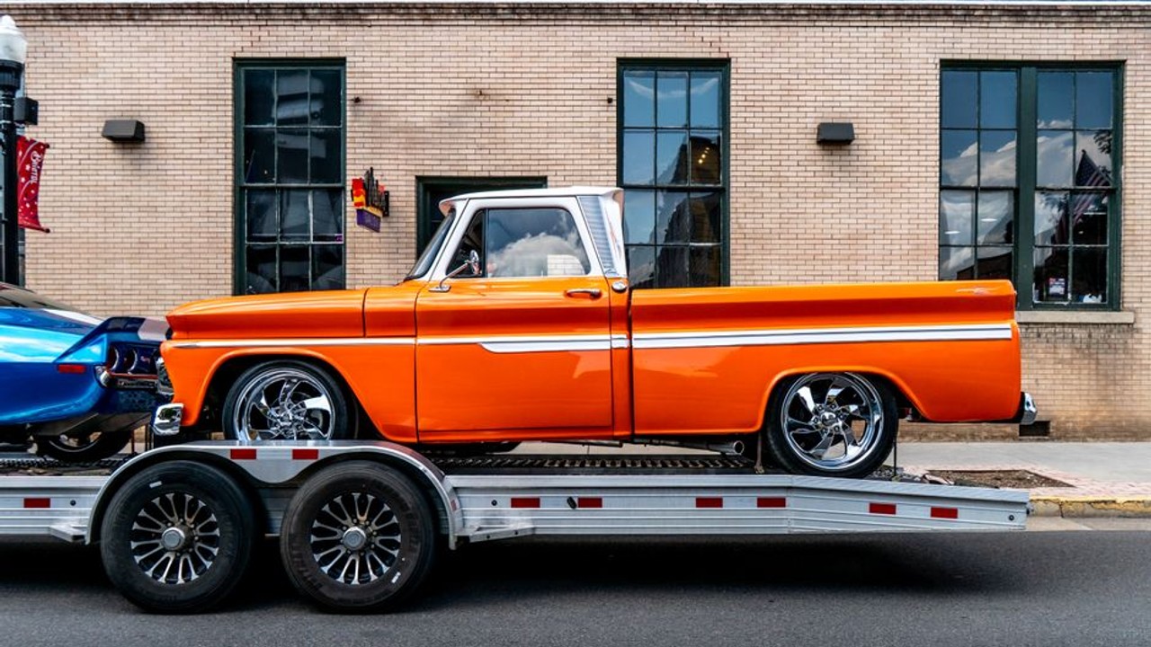 Enclosed car carrier truck carefully loading a vintage classic car onto its ramp, showcasing specialized auto transport for luxury vehicles
