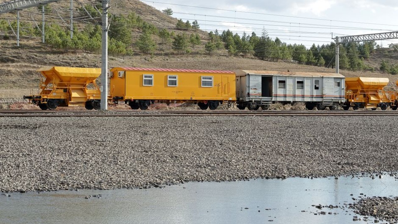 long train carrying multiple cars on flat tracks through a scenic landscape