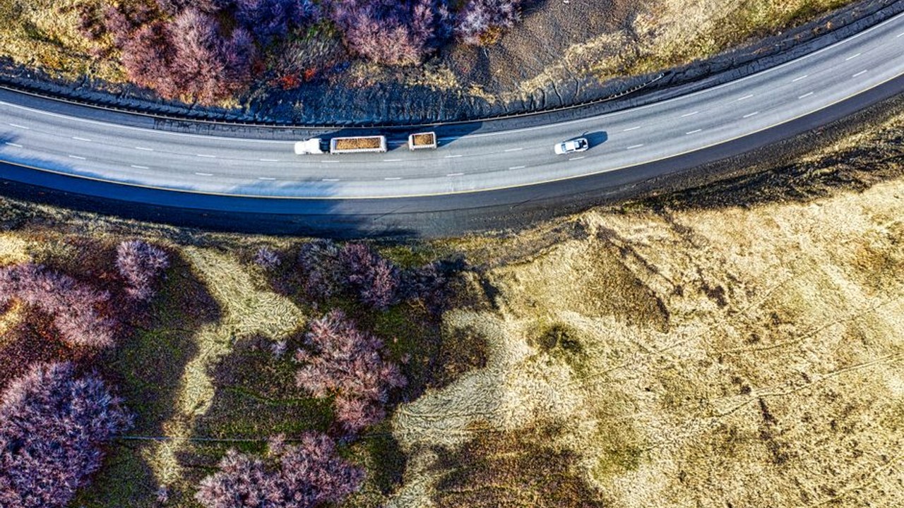 aerial view of a multi-level car carrier truck navigating a winding highway through mountains