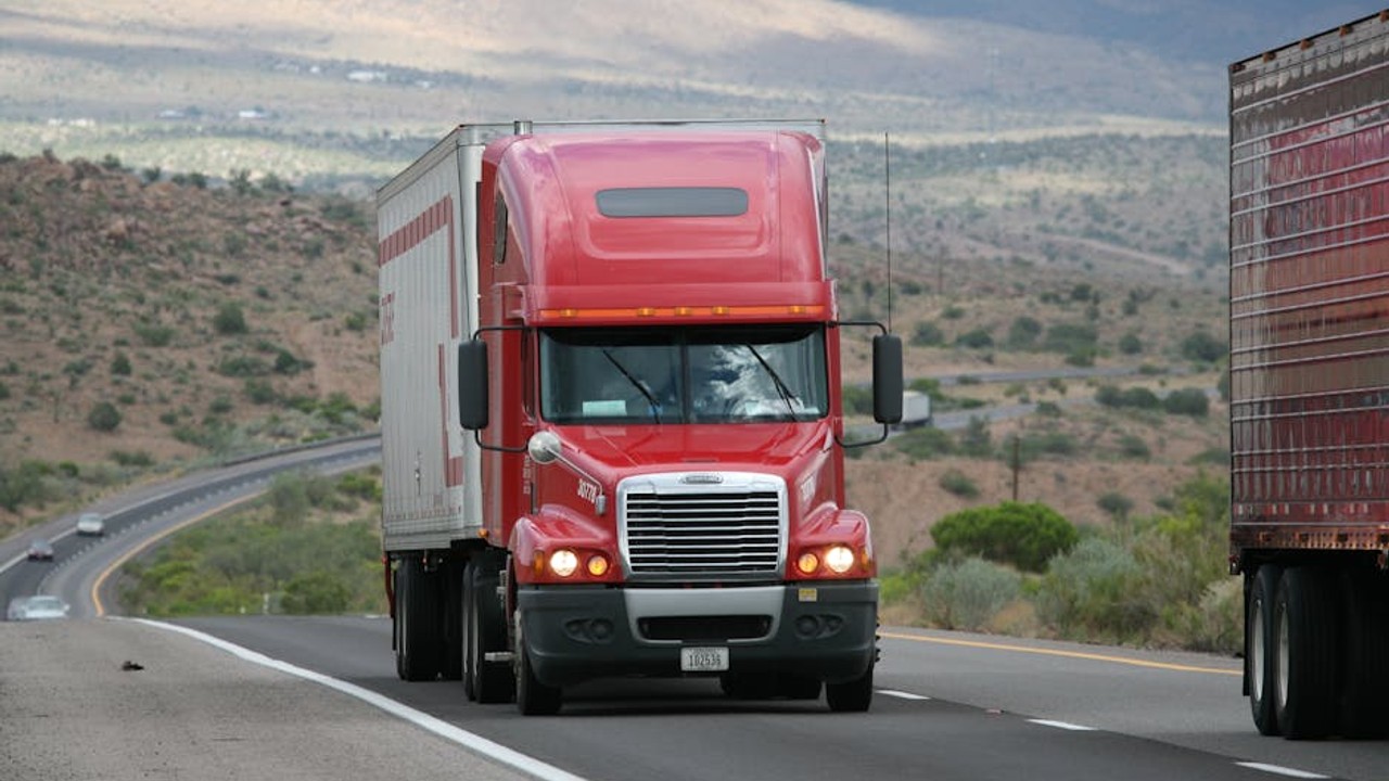 Large car carrier truck with multiple vehicles driving on a sunny interstate highway, illustrating cross country shipping