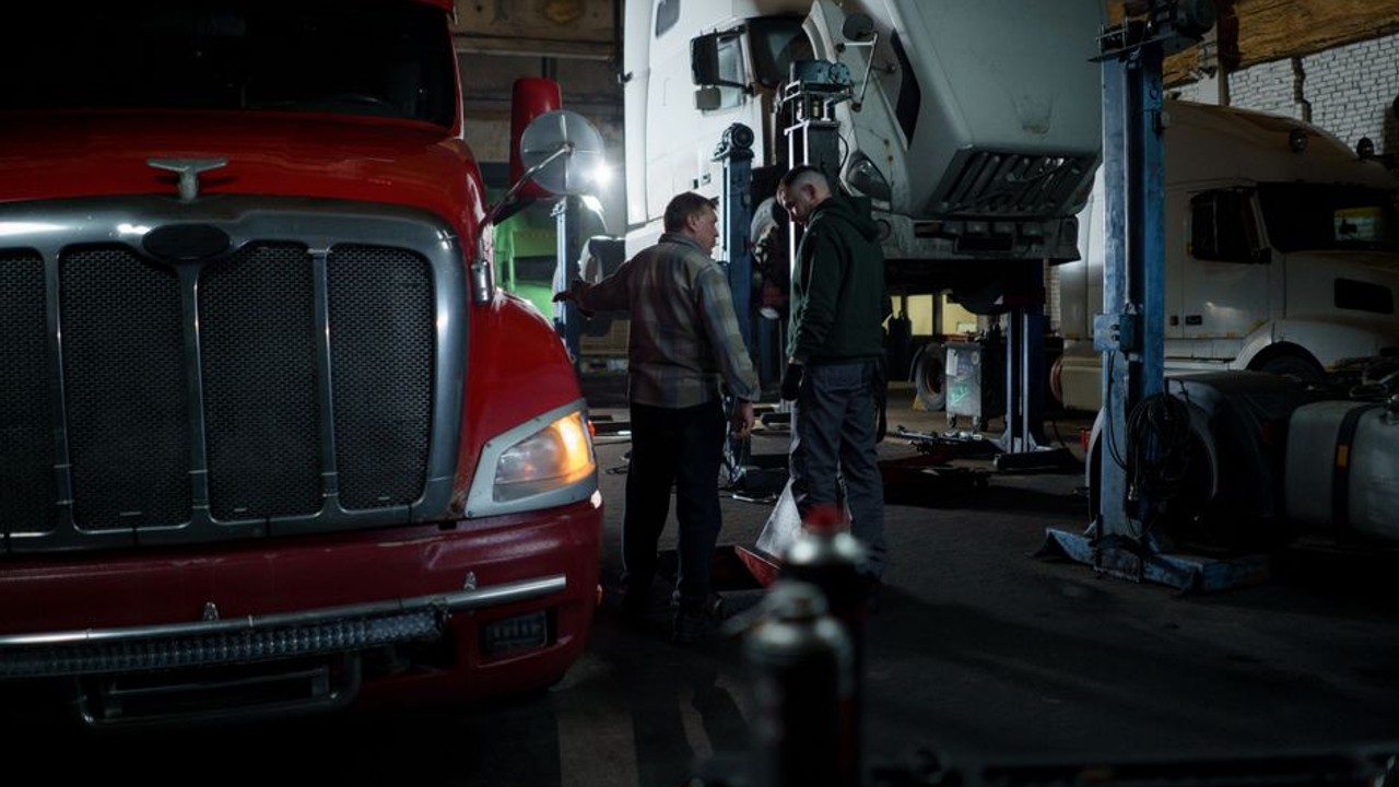 Driver conducting a final inspection of a car on a hydraulic lift of an auto transport truck, checklist in hand