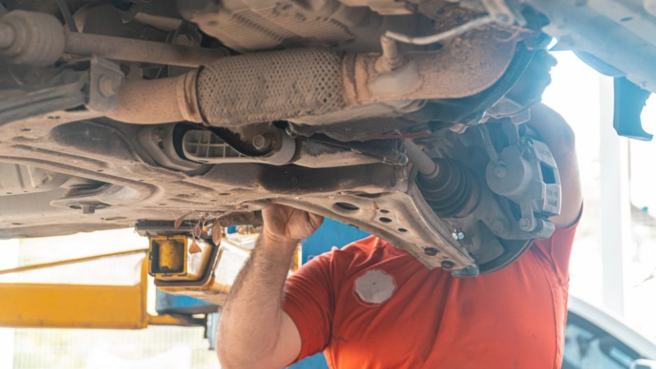 Professional car carrier driver carefully inspecting a vehicle's undercarriage for fluid leaks before loading it onto an open auto transport trailer