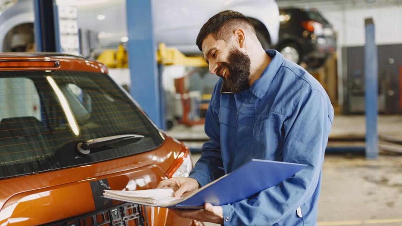 A mechanic explaining a repair estimate to a car owner via video call, demonstrating remote repair coordination for a vehicle stranded mid-route during transport