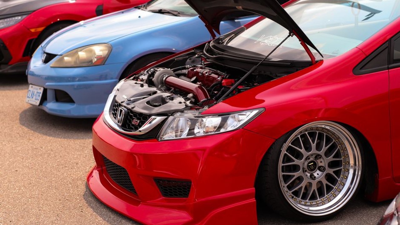 Enclosed car carrier truck meticulously loading a lowered sports car with custom bodywork and aftermarket wheels, highlighting the careful handling required.