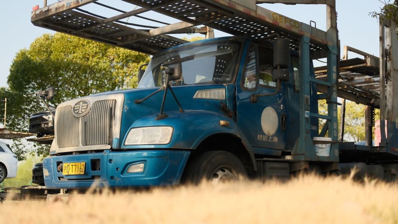 Professional car hauler securing a blue sedan onto the lower deck of a multi-car open transport truck, ensuring safety for long-distance travel